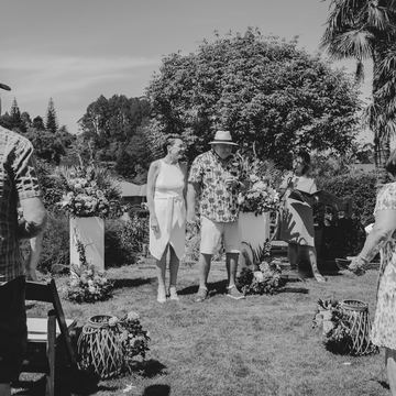 Black-and-white photo of the bride and groom walking down a garden aisle as guests turn to watch
