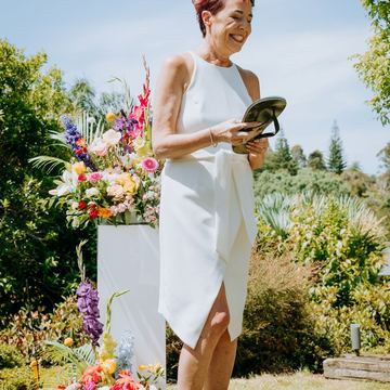 The bride in a white dress smiling beside a bright floral arrangement in a sunny garden