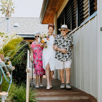 The bride and groom step down from a veranda beside a white weatherboard house