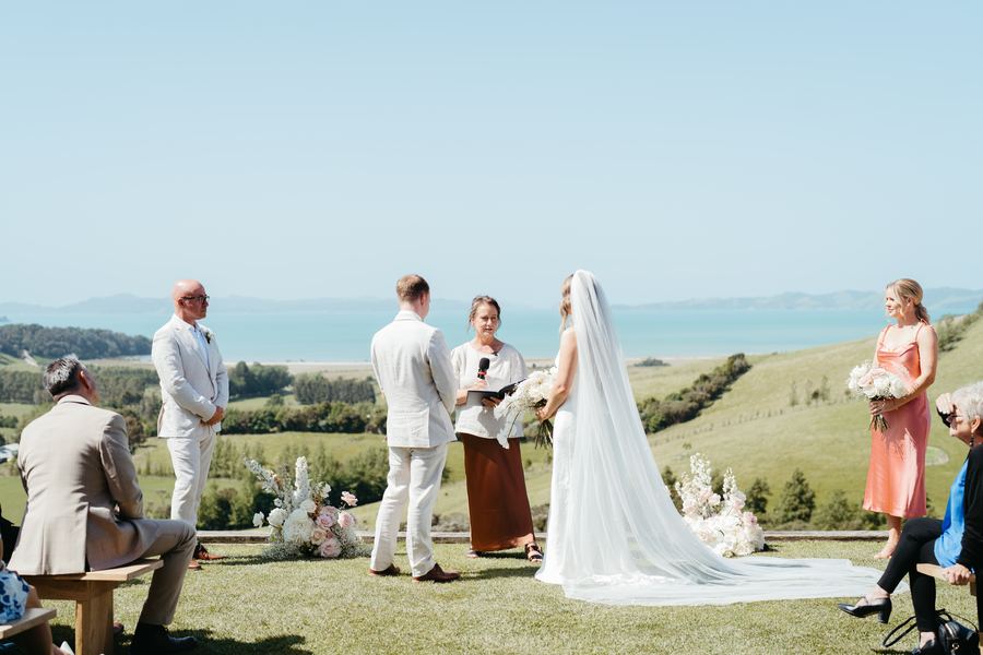 The bride and groom stand before Tracy with guests and bridesmaids around them
